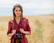 young woman in red dress with camera on wheat field