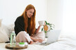 Redhead young woman sitting in bedroom and doing online shopping. Girl looking at laptop and buying natural beauty cosmetic products by the internet at home.