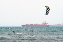 Kitesurfing During A Windy Day With A Very Rough Sea And Industrial Boat In The Background