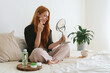 © valeriyakozoriz - Red hair young girl doing beauty routine with gua sha quartz roller at home. Redhead beautiful woman using facial massage natural stone in bedroom. Beauty routine and skincare concept.