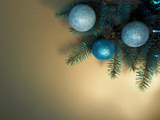 a blue and two gray Christmas balls are lying on a branch of a blue Christmas tree on a beige background. top view. copy space