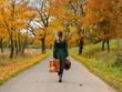 Woman in green cloak with suitcase on countryside road in autumn season time