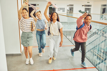 Wall Mural - Full length portrait of multi-ethnic group of schoolkids holding masks and smiling happily while walking towards camera indoors