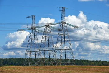 high voltage power line towers against the background of cumulus clouds and blue summer sky