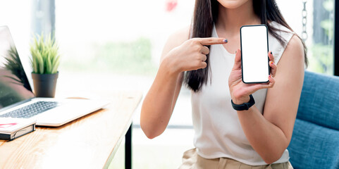 Wall Mural - cropped shot of woman hand holding smartphone and showing blank screen while sitting at the table at
