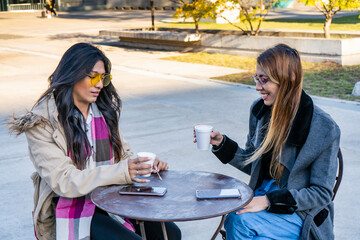 Young latin women drinking coffee in a cafe outdoors in sunny day.