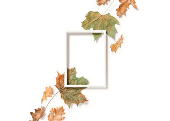 Wall Mural - Minimalistic autumn composition. An empty photo frame and diagonal maple and oak leaves are on a white background. Flat lay. Top view. Copy space.