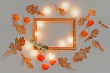 Wall Mural - Creative autumn layout. An empty wooden photo frame is illuminated with a glowing garland. The template is decorated with dried oak leaves and flowers. Flat lay. Copy space.