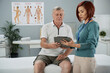 © DragonImages - Female physiotherapist talking to senior patient in medical office and explaining him details of therapy
