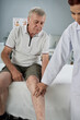 © DragonImages - Physiotherapist checking injured leg of senior patient before performing physical therapy in medical office