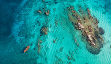 View From Above, Stunning Aerial View Of A Wooden Boat Anchored To Some Rocks Bathed By A Crystal Clear, Turquoise Water. Giardinelli Island, La Maddalena Archipelago, Sardinia, Italy.