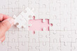 © sorapop - Top view flat lay of hand-holding last piece white paper jigsaw puzzle game last pieces put to place for solve problem complete mission, studio shot on a pink background, quiz calculation concept