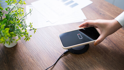 Wall Mural - Charging mobile phone battery with wireless charging device in the table. Smartphone charging on a charging pad. Mobile phone near wireless charger Modern lifestyle technology concept.