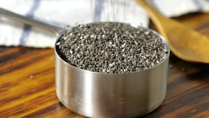 Wall Mural - Pouring black chia seeds into a stainless steel measuring cup
