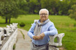 © Studio Romantic - Senior man stands in the park with a book in his hands. An elderly man in glasses, a scarf and white hair stands in the park. Green grass, summer.