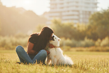 Embracing the pet. Woman with her dog is having fun on the field at sunny daytime