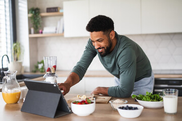 Wall Mural - Young man with tablet preparing healthy breakfast indoors at home, home office concept.