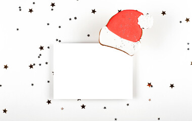 Wall Mural - White empty Christmas card and gingerbread Santa hat on light background with gold stars. Minimalistic mock up layout