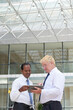 © DragonImages - Positive mature business people standing in hall of office building and discussing chart on tablet computer