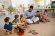 © Halfpoint - Group of small nursery school children with man teacher sitting on floor indoors in classroom, playing musical instruments.