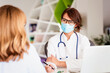 © sepy - Female doctor wearing face mask and consulting her patient while sitting at desk in doctor's office