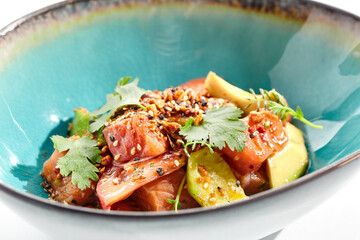 Poster - Salmon and avocado salad bowl. Blue salad bowl isolated on white background. Salad garnished with micro greens and sesame, chopped salmon, sliced avocado and parsley green leaf. Raw salmon