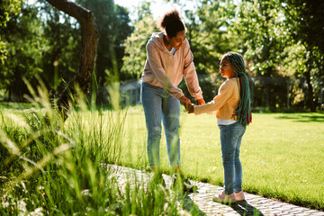 Wall Mural - Black woman and her daughter talking while walking in green park