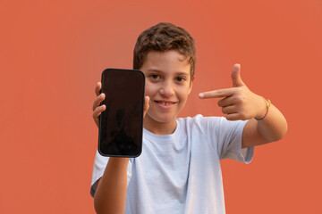 Young caucasian little boy showing a smartphone display screen. Useful for layout app or website advertisement. Looking at camera.