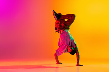 Wall Mural - Portrait of young stylish man, break dancing dancer training in casual clothes isolated over gradient pink yellow background at dance hall in neon light.