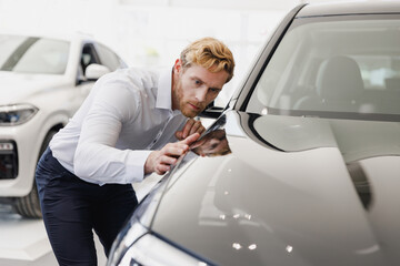 Canvas Print - Man customer male buyer client wears white shirt chooses auto wants to buy new automobile in car showroom look at perfect glossy hood vehicle salon dealership store motor show indoor. Sales concept.