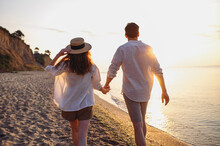 Back Rear View Young Lovely Couple Two Friends Family Man Woman 20s In White Shirt Clothes Hold Hands Walk Stroll Together At Sunrise Over Sea Beach Ocean Outdoor Exotic Seaside In Summer Day Evening.