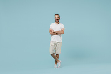 Wall Mural - Full length young smiling friendly cheerful happy man 20s wearing casual white t-shirt looking camera hold hands crossed folded isolated on plain pastel light blue color background studio portrait