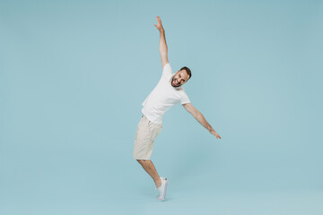 Wall Mural - Full length young smiling happy man 20s in white t-shirt leaning back with outstretched hand dancing fooling around stand on toes isolated on plain pastel light blue color background studio portrait