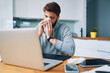© baranq - Sick man blowing nose while working from home