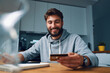 © baranq - Smiling young man making online payments at home with credit card and laptop