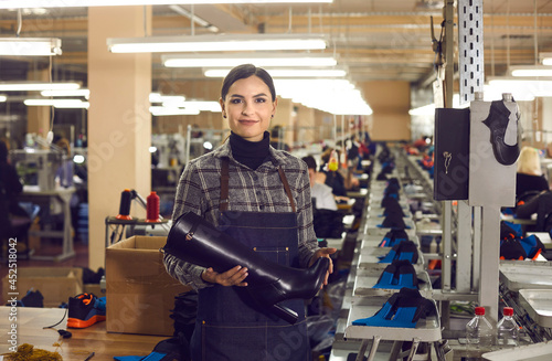 Portrait of a happy female shoe factory worker holding a women\'s heeled boot from the new collection of classic black leather women\'s shoes. Concept of production of quality shoes for women.