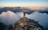 Fototapeta Na sufit - A hiker stands on the ridge watching the valley being flooded by clouds at sunset. Traveling in mountains. Adventure, Art, Travel and Hike concept.