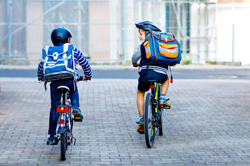 Two school kid boys in safety helmet riding with bike in the city with backpacks. Happy children in colorful clothes biking on bicycles on way to school. Safe way for kids outdoors to school