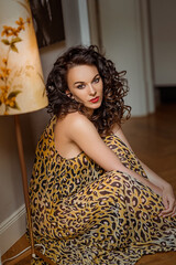 Poster - Beautiful Caucasian curly woman wearing a leopard pattern long dress sitting on