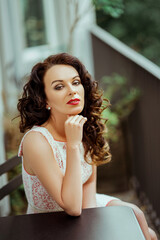 Wall Mural - Curly Caucasian brunette woman wearing a dress sitting behind the table