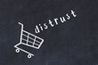 Chalk drawing of shopping cart and word distrust on black chalboard. Concept of globalization and mass consuming