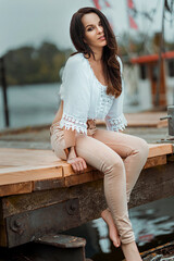 Wall Mural - Beautiful Caucasian brunette woman wearing a white top and pink pants sitting in the port