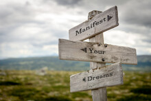Manifest Your Dreams Text Quote On Wooden Signpost Outdoors In Nature.