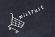 Chalk drawing of shopping cart and word mistrust on black chalboard. Concept of globalization and mass consuming