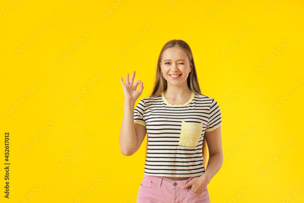 Young woman showing OK on color background