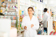 © JackF - Female pharmacist standing with drug package in salesroom of drugstore. Her colleague standing behind.