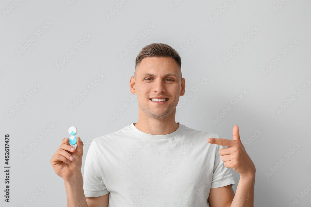 Young man with contact lenses on light background