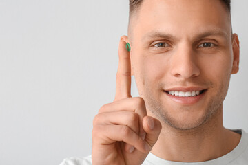 Wall Mural - Young man putting in contact lens on light background