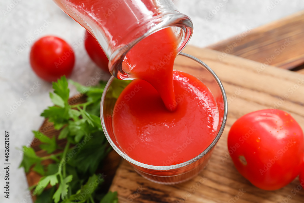Pouring tasty tomato juice from bottle into glass on light background