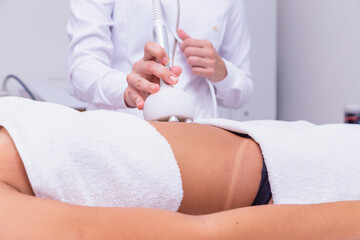 Wall Mural - Cropped shot of a professional dermatologist performing radiofrequency lifting procedure on the stomach of a woman. Female client getting rf-lifting treatment on her belly at cosmetology clinic.